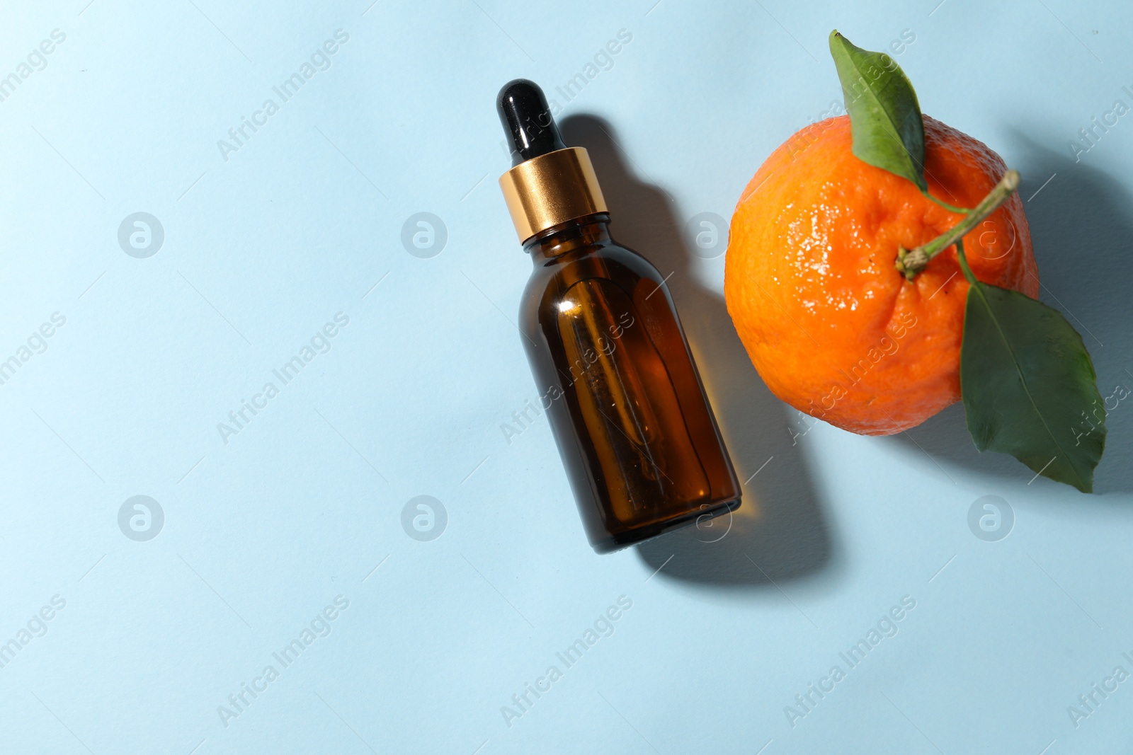Photo of Aromatic tangerine essential oil in bottle and citrus fruit on light blue table, top view. Space for text
