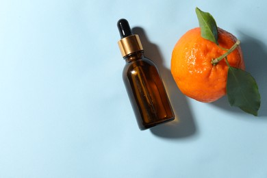 Aromatic tangerine essential oil in bottle and citrus fruit on light blue table, top view. Space for text