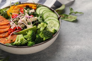 Bowl with many different vegetables and tofu on grey table, closeup and space for text. Vegan diet