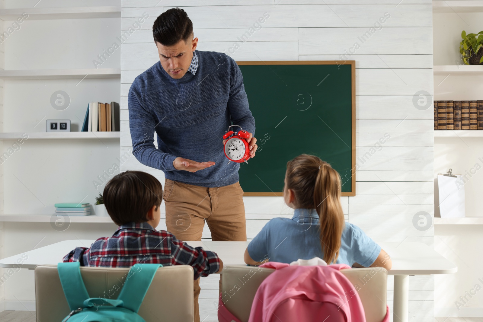 Photo of Teacher with alarm clock scolding pupils for being late in classroom