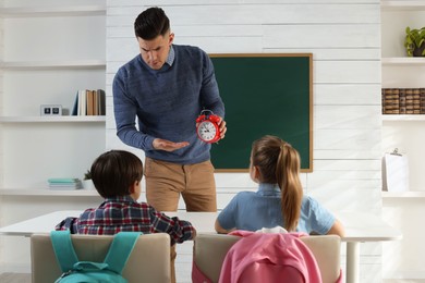 Photo of Teacher with alarm clock scolding pupils for being late in classroom