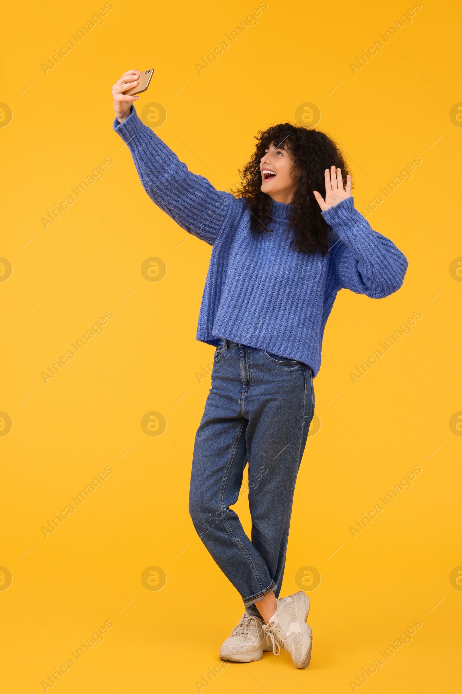 Photo of Beautiful young woman taking selfie with smartphone on orange background