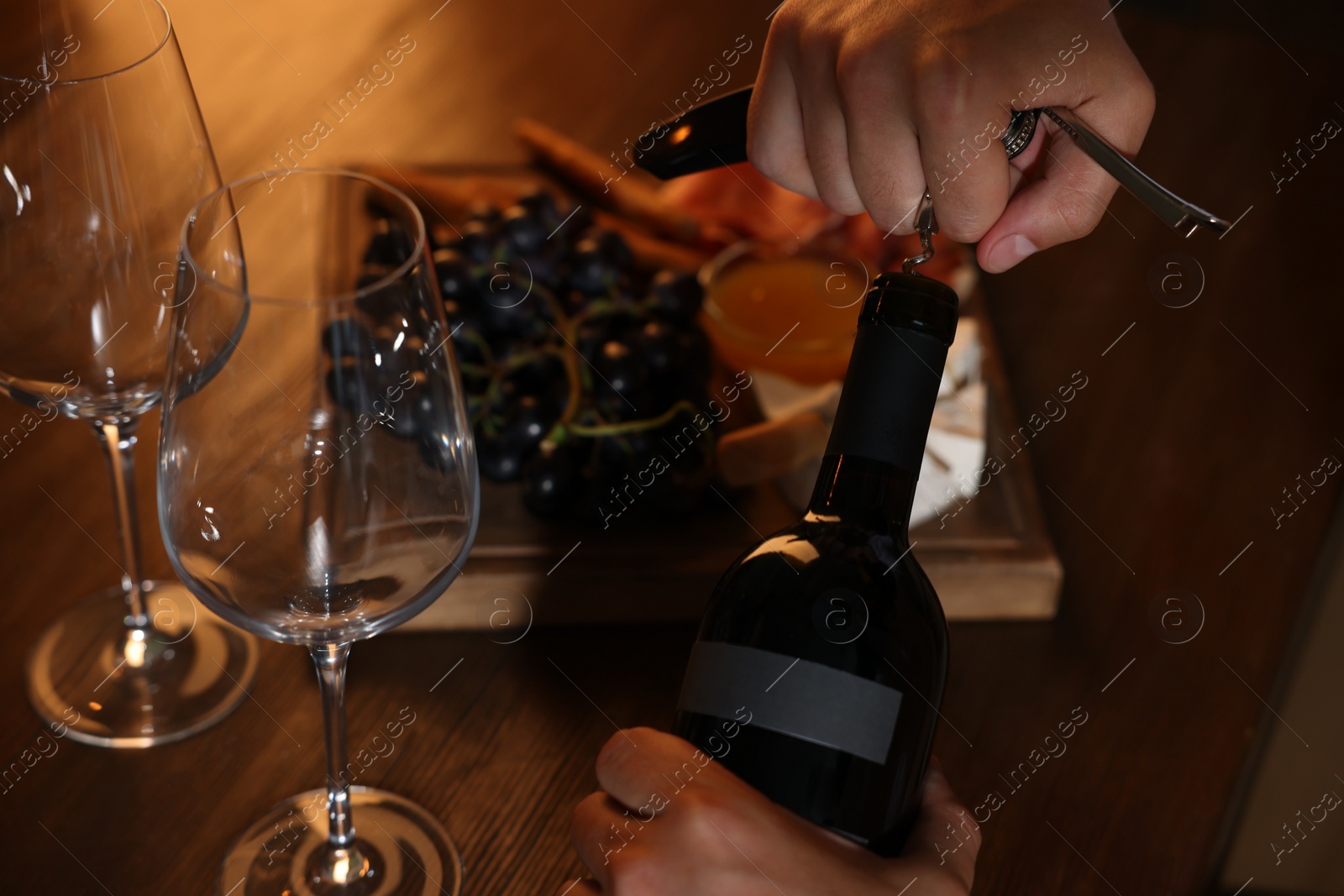 Photo of Romantic dinner. Man opening wine bottle with corkscrew at table, closeup