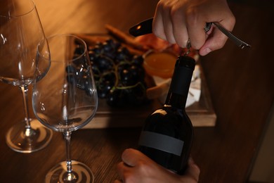 Photo of Romantic dinner. Man opening wine bottle with corkscrew at table, closeup