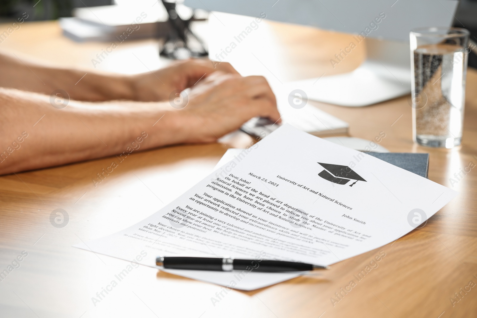 Photo of Student using computer at wooden table indoors, focus on acceptance letter from university