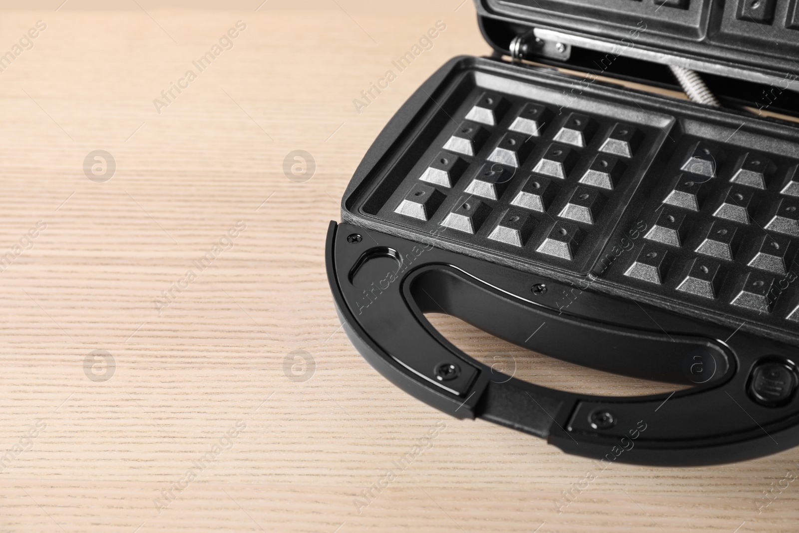 Photo of Modern waffle iron on wooden table, closeup