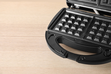 Photo of Modern waffle iron on wooden table, closeup