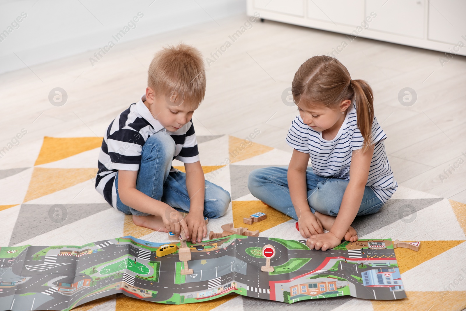 Photo of Little children playing with set of wooden road signs and toy cars indoors