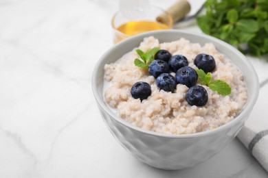 Photo of Delicious barley porridge with blueberries and mint in bowl on white marble table, closeup. Space for text