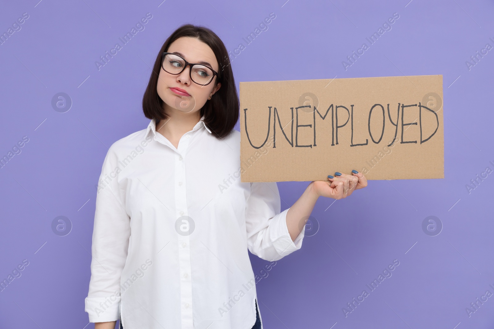 Photo of Young woman holding sign with word Unemployed on violet background