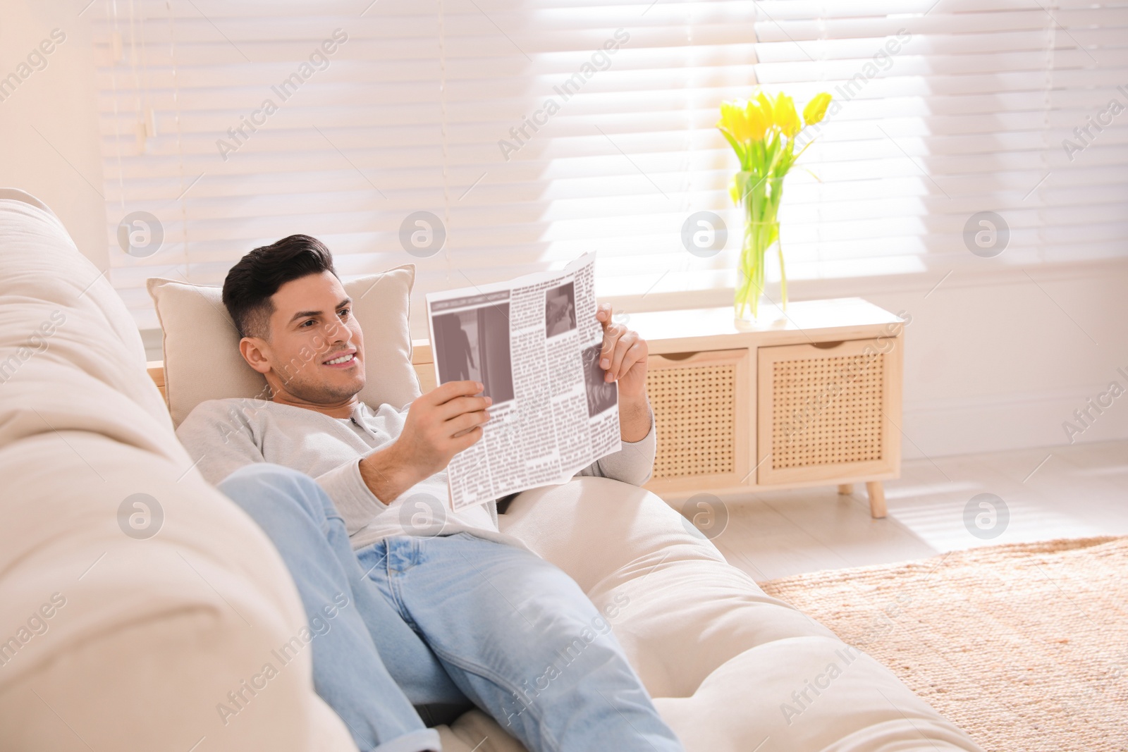 Photo of Man reading newspaper on sofa at home