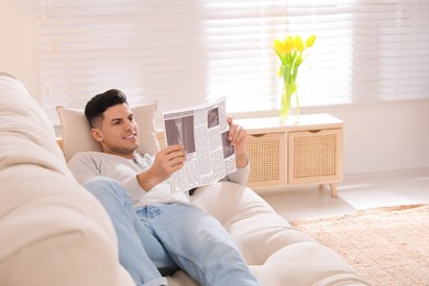 Man reading newspaper on sofa at home