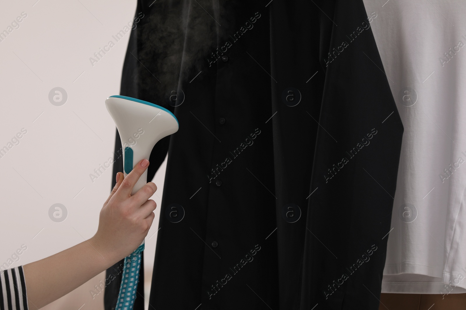 Photo of Woman steaming black shirt on white background, closeup