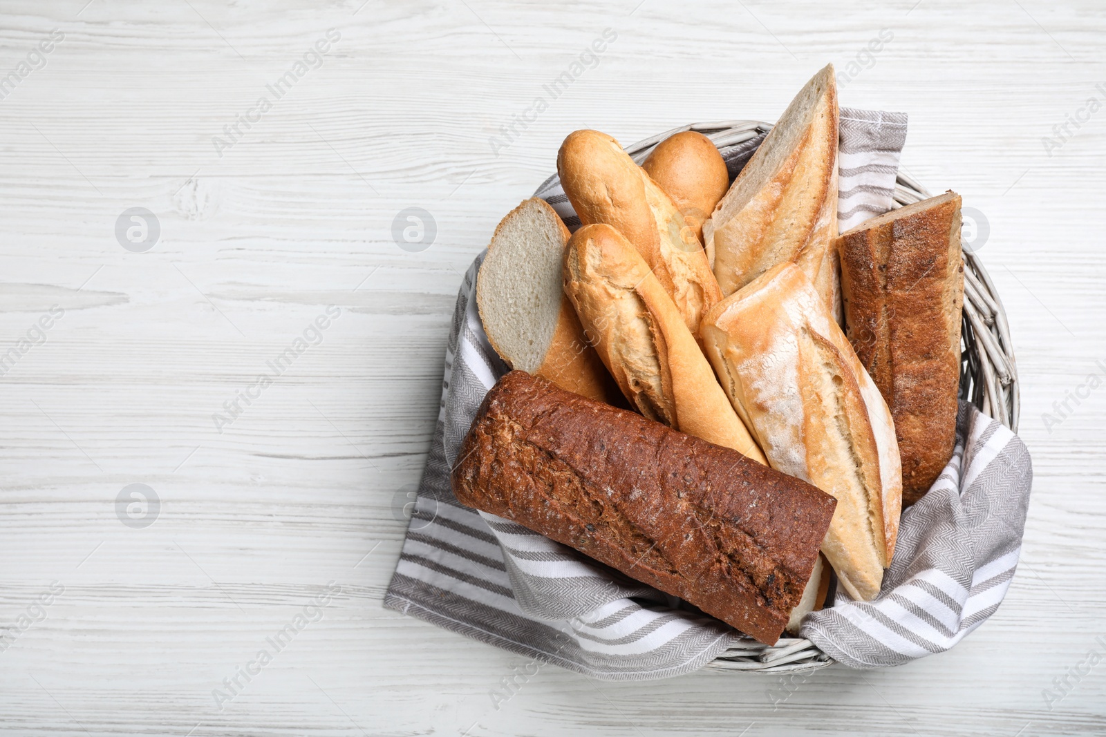 Photo of Different tasty baguettes in basket on white wooden table, top view. Space for text