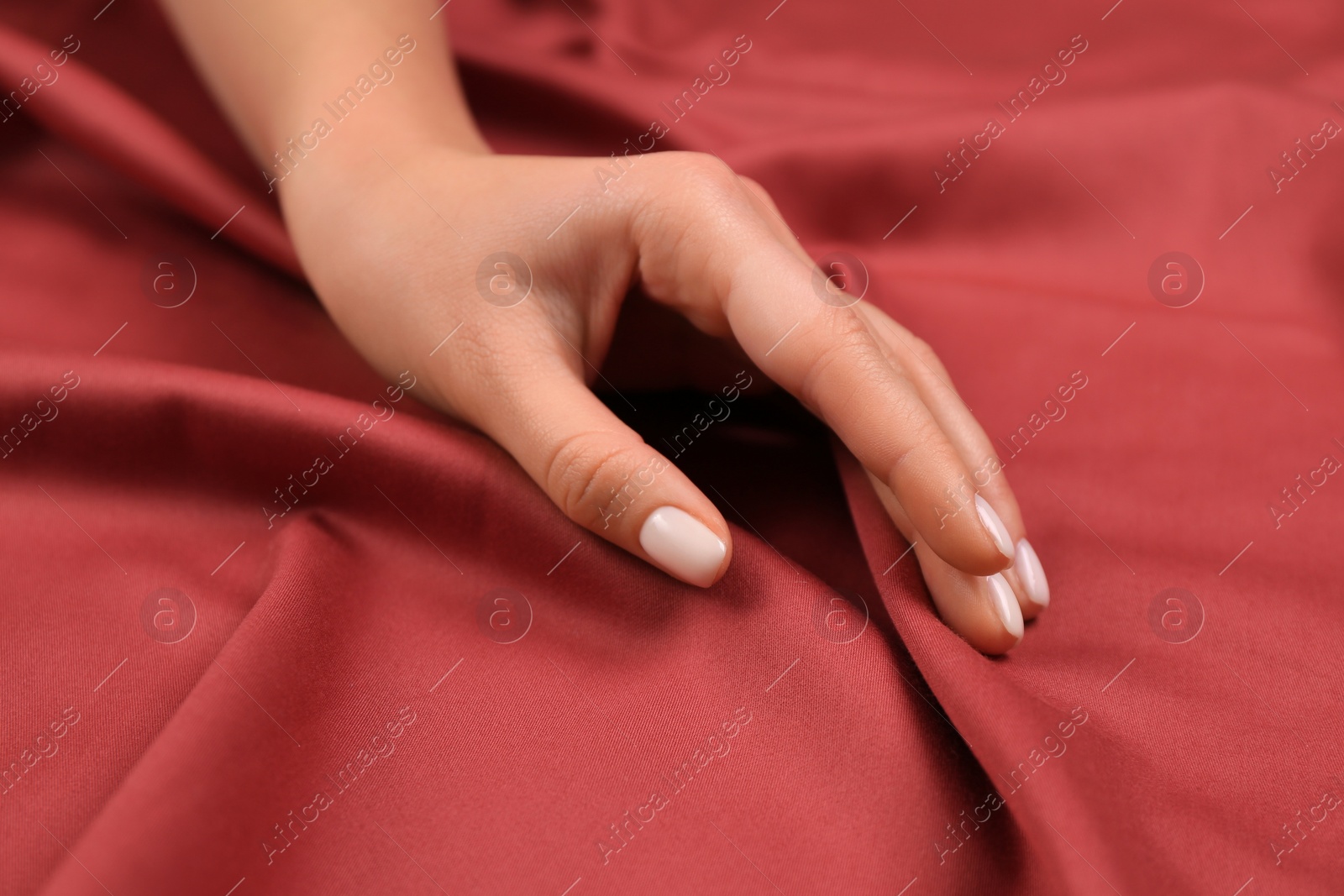 Photo of Woman touching smooth dark red fabric, closeup