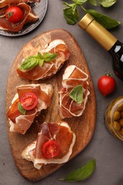 Tasty sandwiches with cured ham, basil and tomatoes on grey textured table, flat lay