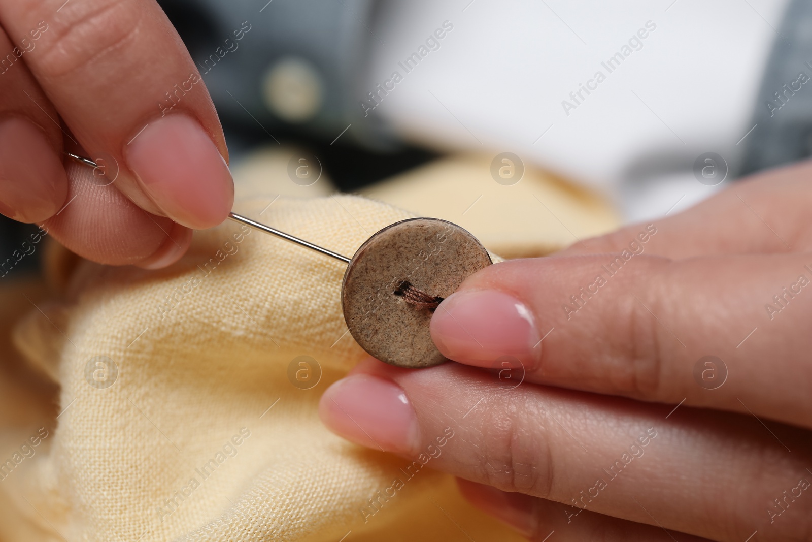 Photo of Woman sewing button with needle and thread onto shirt, closeup