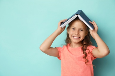 Portrait of cute girl with book on turquoise background, space for text. Reading concept