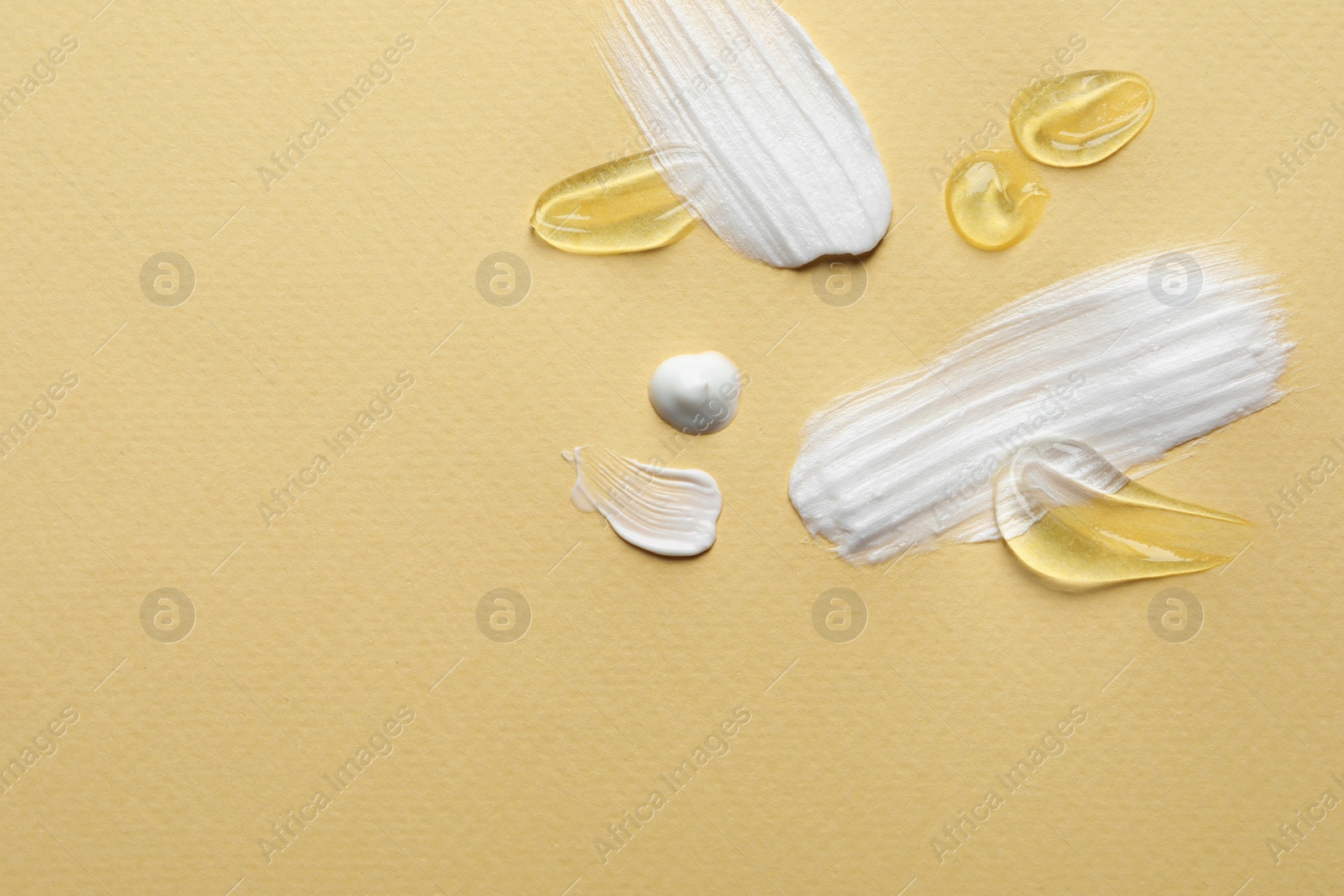 Photo of Samples of transparent gel and white cream on yellow background, flat lay. Space for text