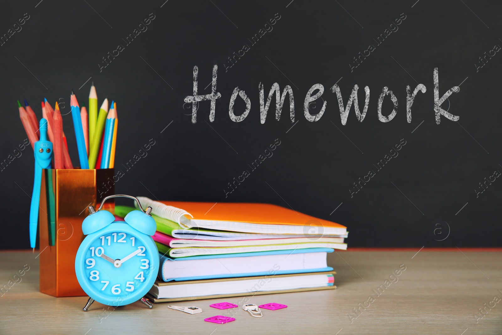 Image of Composition with stationery and alarm clock on table near blackboard. Doing homework