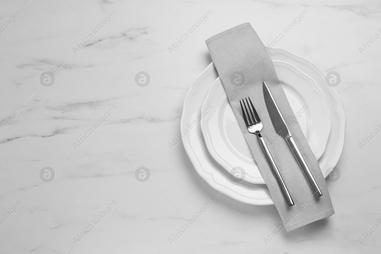 Photo of Clean plates with shiny silver cutlery on white marble table, flat lay. Space for text