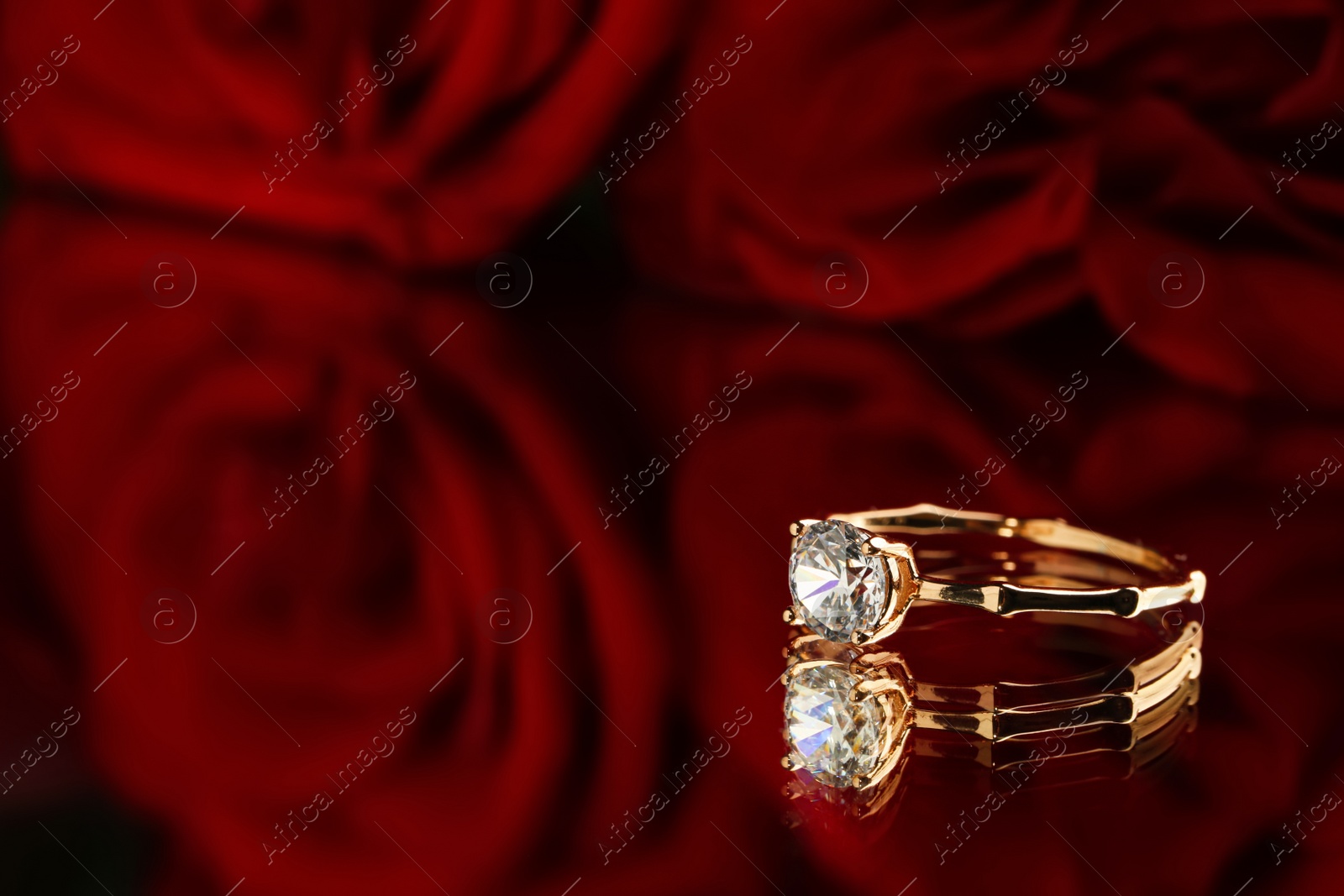 Photo of Beautiful engagement ring with gemstone and roses on mirror, closeup. Space for text