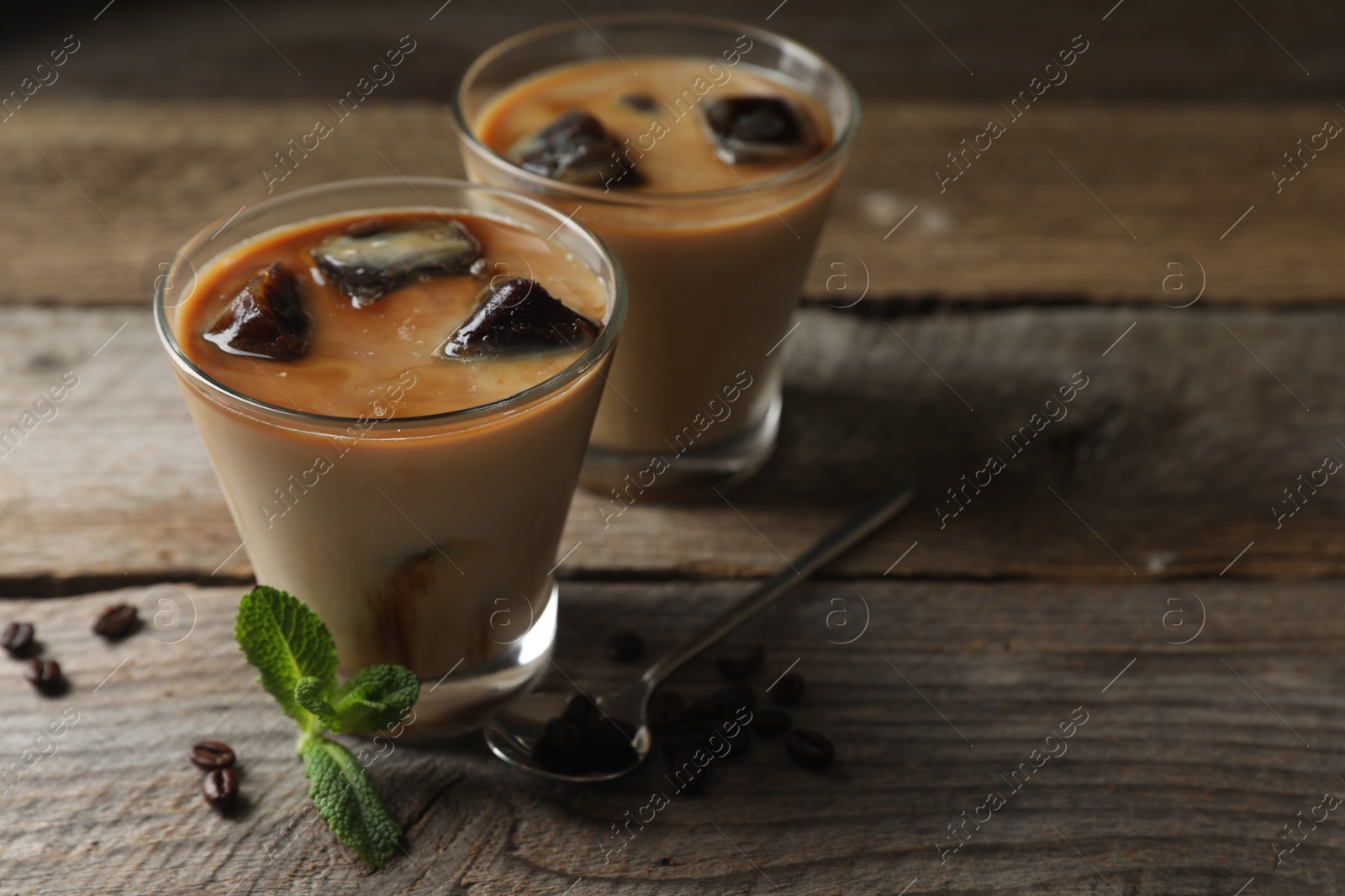 Photo of Glasses of delicious iced coffee with milk, beans and mint on wooden table, space for text