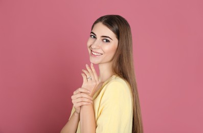 Happy young woman wearing beautiful engagement ring on pink background