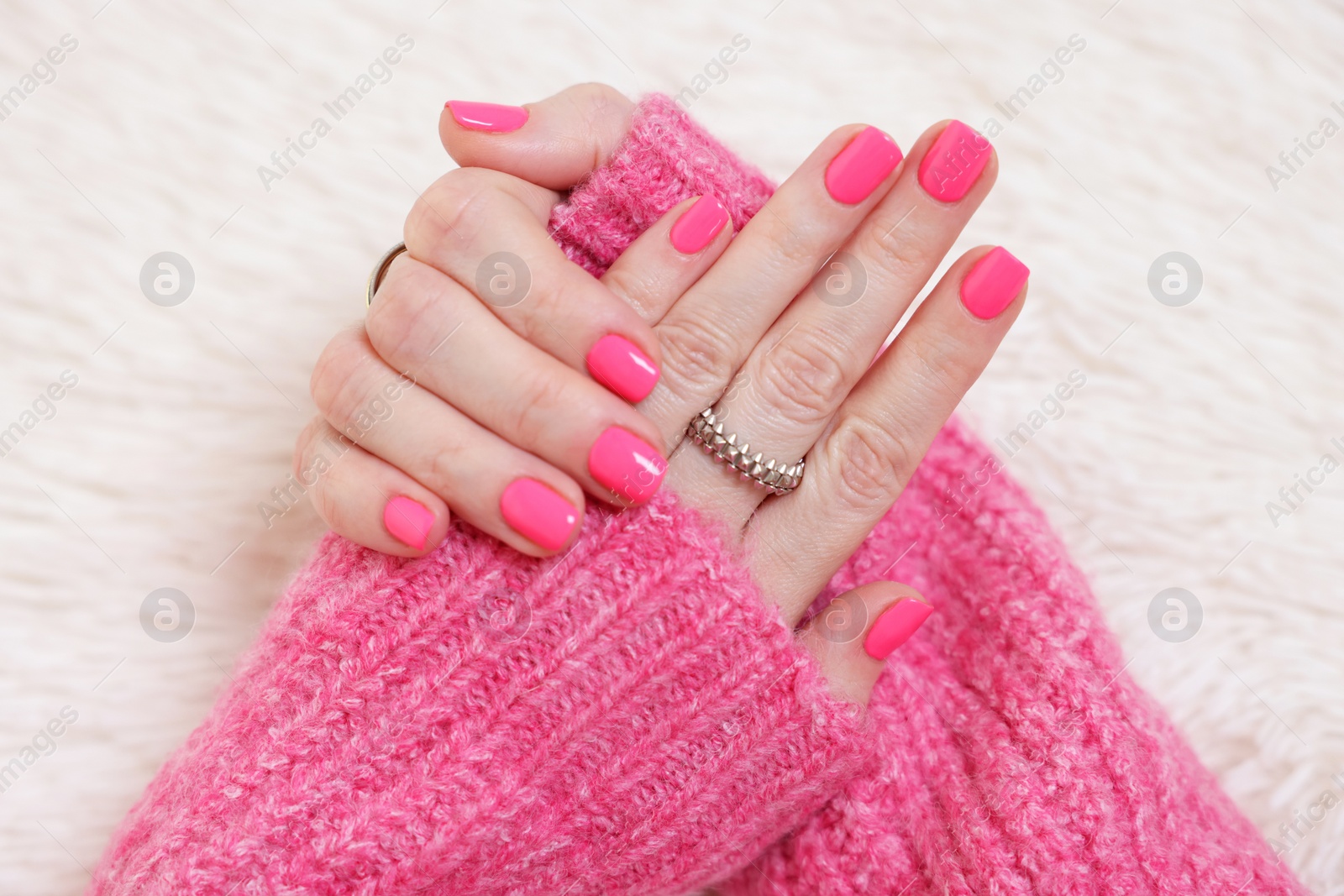 Photo of Woman showing her manicured hands with pink nail polish on faux fur mat, closeup