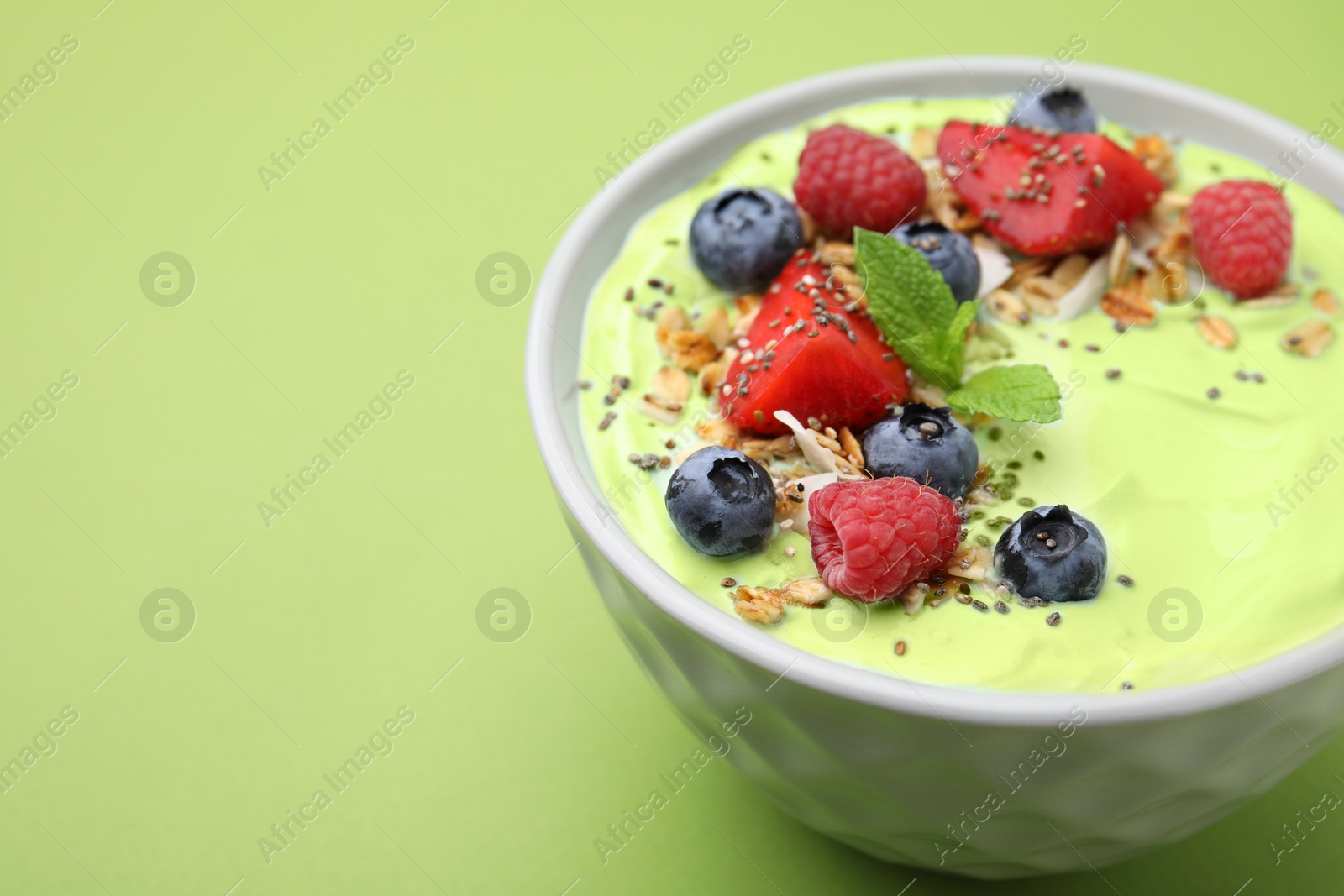 Photo of Tasty matcha smoothie bowl served with berries and oatmeal on green background, closeup with space for text. Healthy breakfast