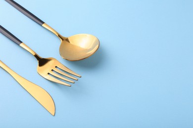 Photo of Stylish golden cutlery set on light blue background, closeup. Space for text
