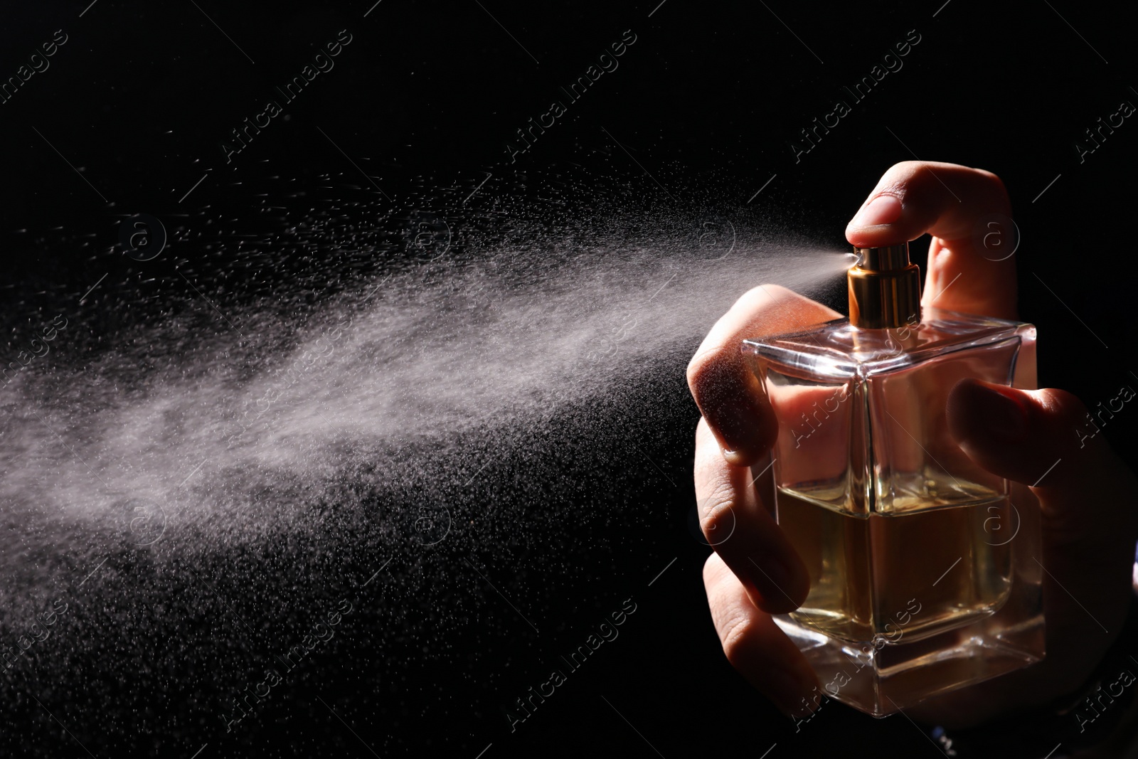 Photo of Man spraying luxury perfume on black background, closeup