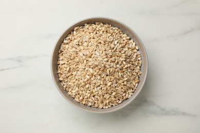 Photo of Dry pearl barley in bowl on white marble table, top view