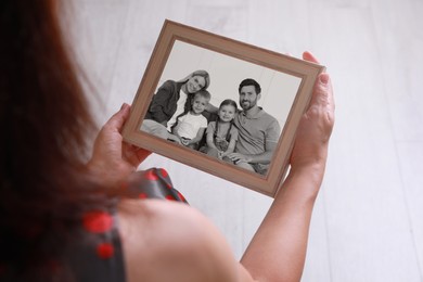 Image of Woman holding frame with black and white photo portrait of her family indoors, closeup
