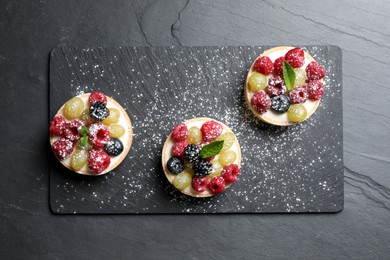 Photo of Delicious tartlets with berries on black table, top view