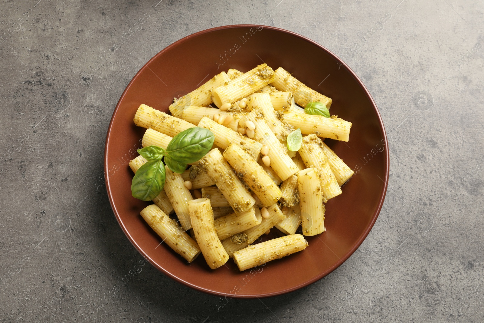 Photo of Plate of delicious basil pesto pasta on grey background, top view