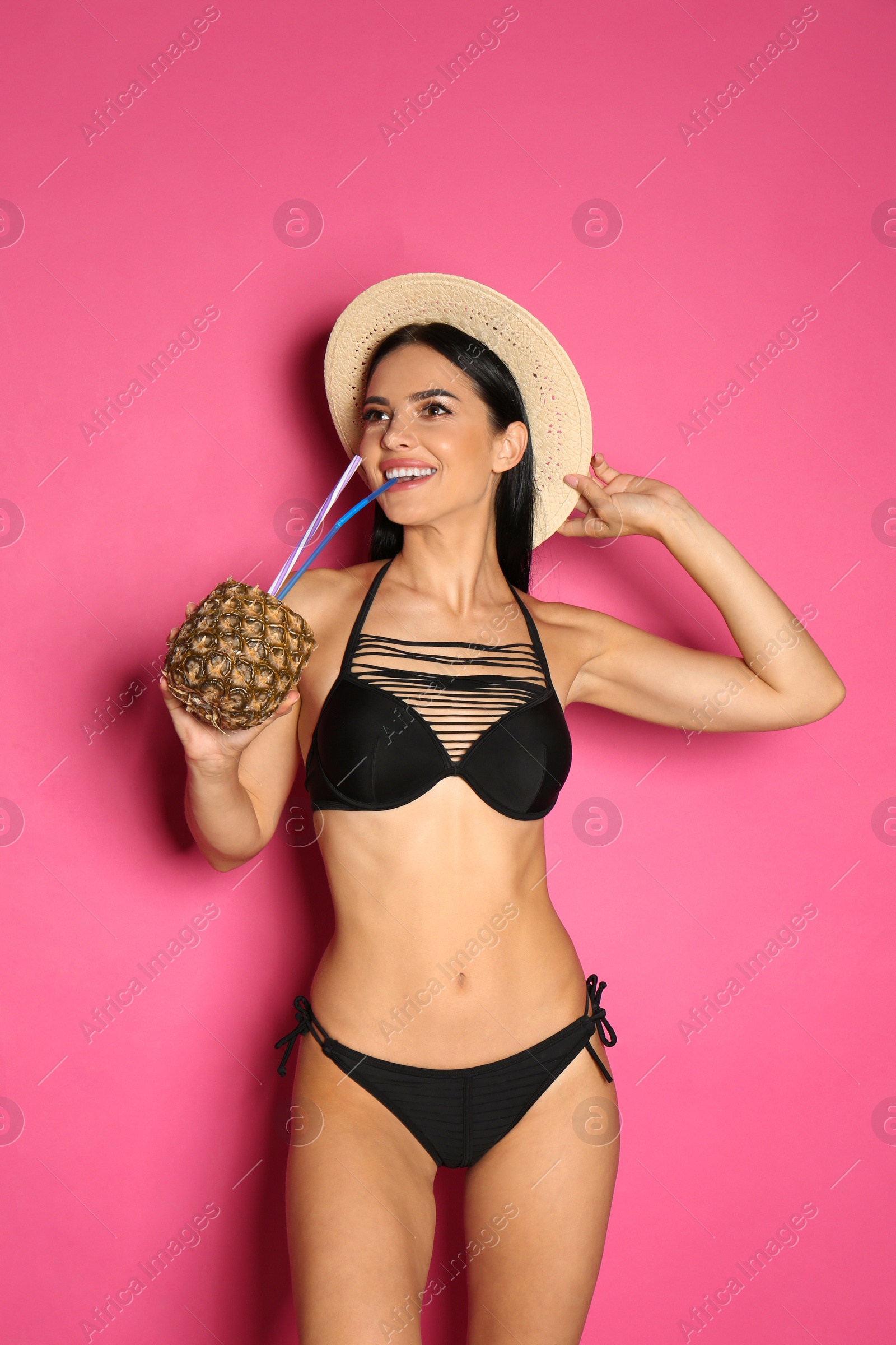 Photo of Beautiful young woman in black bikini with cocktail on pink background
