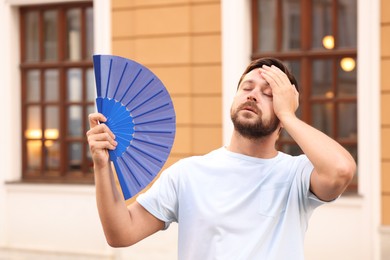 Photo of Man with hand fan suffering from heat outdoors