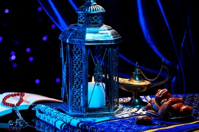 Photo of Arabic lantern, Quran, misbaha, Aladdin magic lamp, dates and folded prayer mat on mirror surface against blurred lights at night