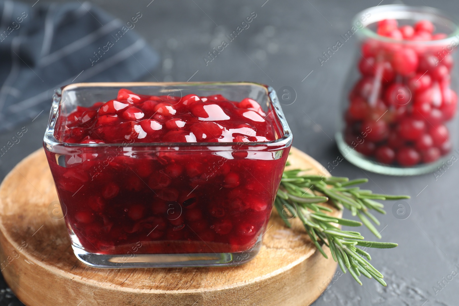 Photo of Fresh cranberry sauce and rosemary in glass bowl on gray table, closeup