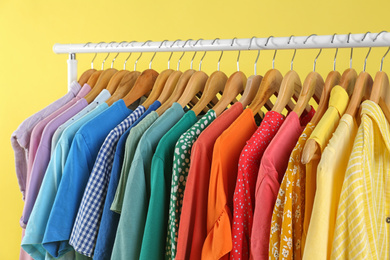 Photo of Bright clothes hanging on rack against yellow background. Rainbow colors