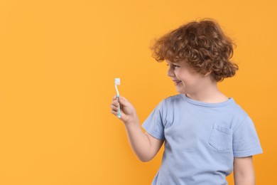 Cute little boy holding plastic toothbrush on yellow background, space for text