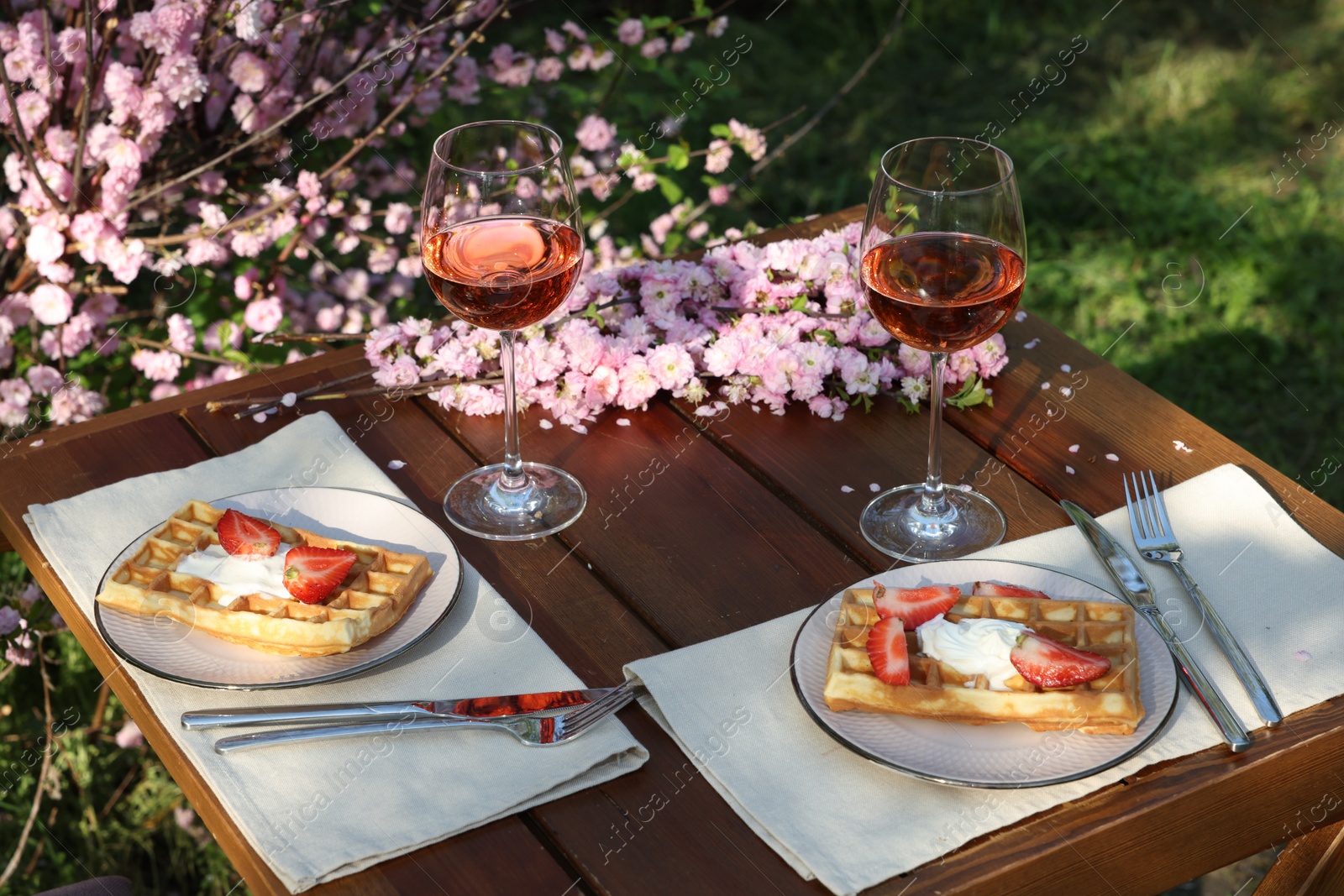 Photo of Delicious Belgian waffles with fresh strawberries and wine served on table in spring garden