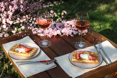 Delicious Belgian waffles with fresh strawberries and wine served on table in spring garden