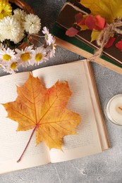 Photo of Books with autumn leaf as bookmark, scented candle and beautiful flowers on light gray textured table, flat lay