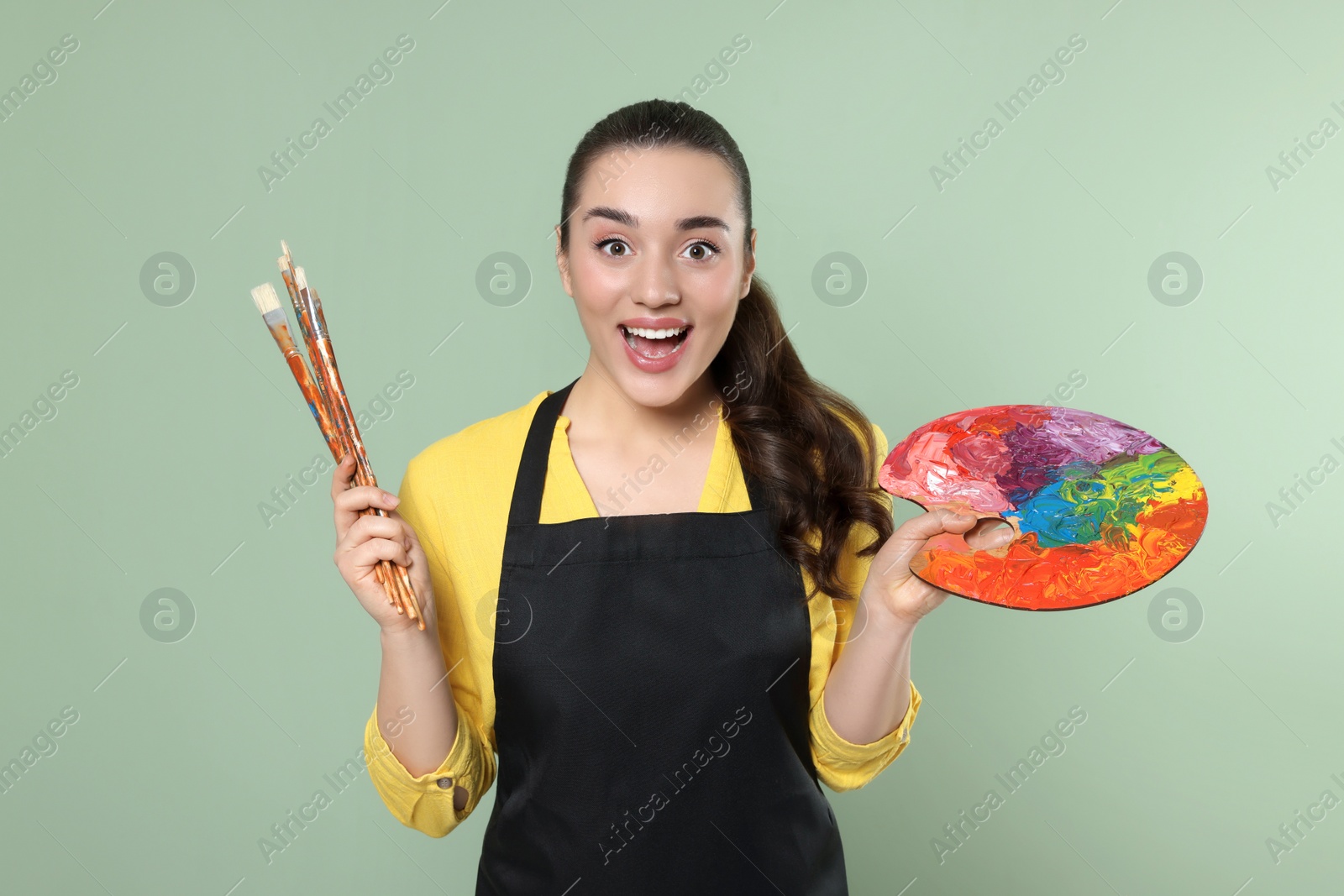 Photo of Woman with painting tools on pale green background. Young artist