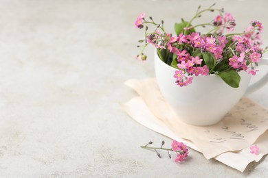 Beautiful pink forget-me-not flowers with cup on light stone table. Space for text