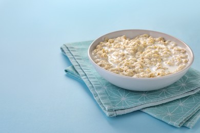 Photo of Tasty boiled oatmeal in bowl on light blue table. Space for text