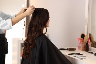 Photo of Hairdresser working with woman using curling hair iron in salon. Space for text