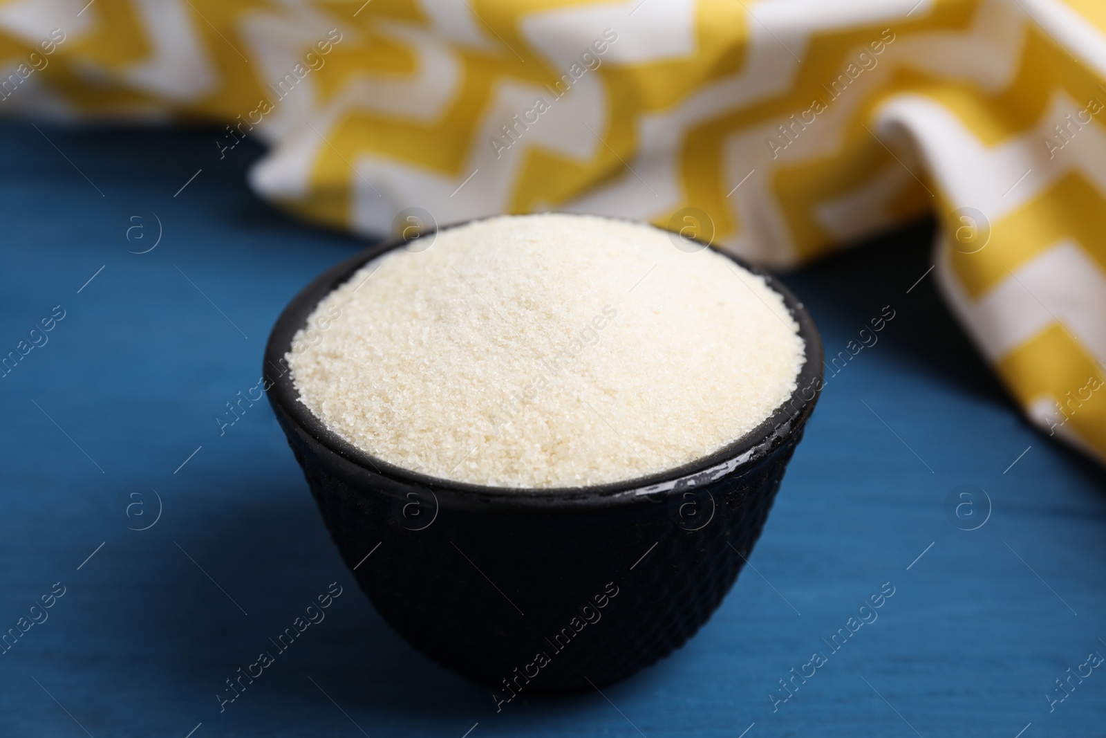 Photo of Gelatin powder in bowl on blue wooden table, closeup